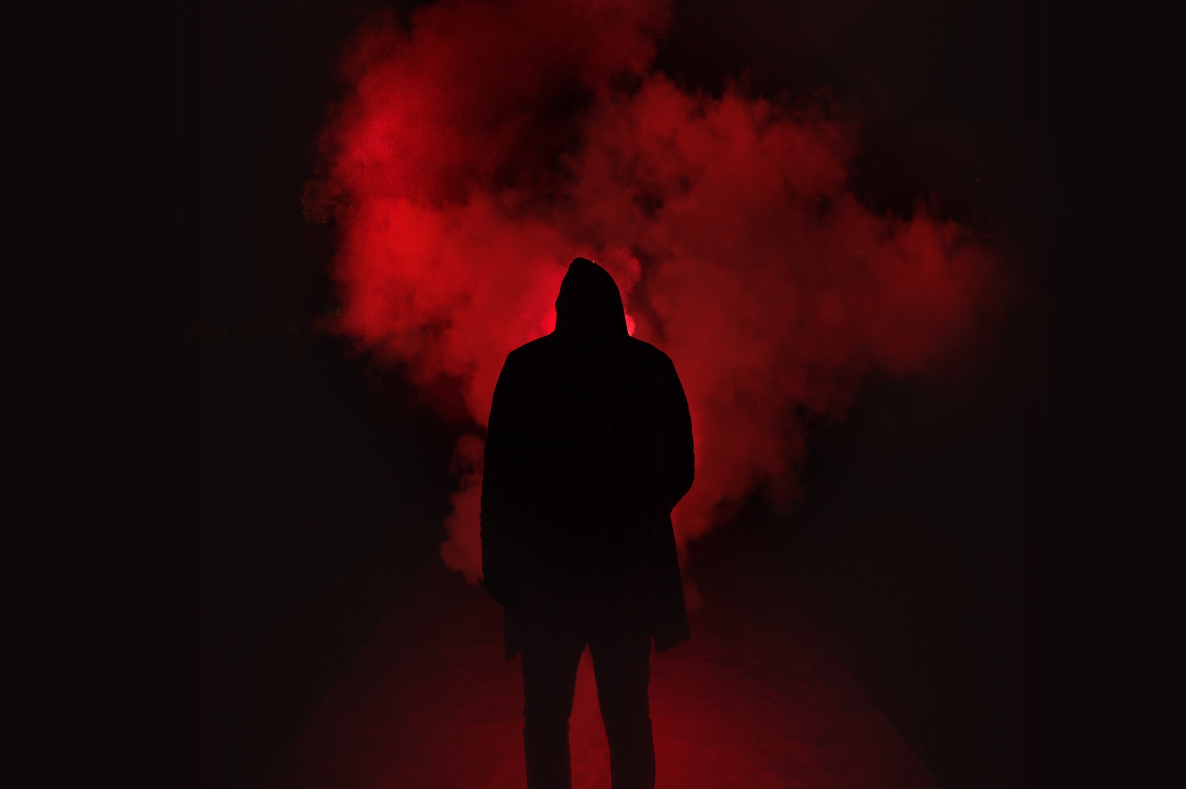 The silhouette of a man wearing a hoodie, on a black backdrop with red smoke.