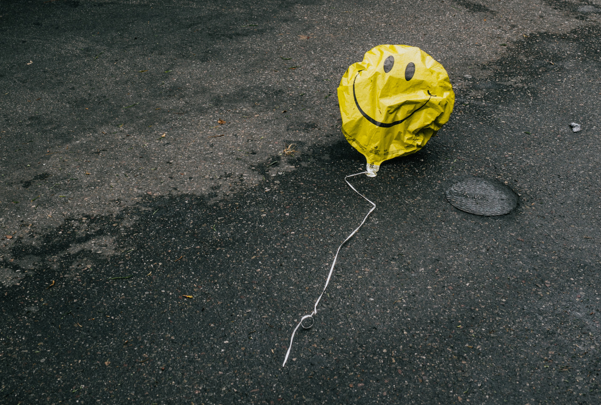 A deflated smiley balloon, lying discarded in the street.