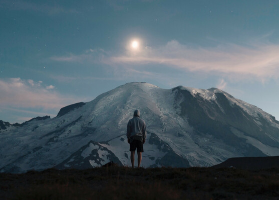 A person wearing a grey hoodie standing in front of a mountain
