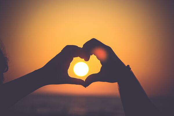 Two hands seen in a sunset, making a heart-shape